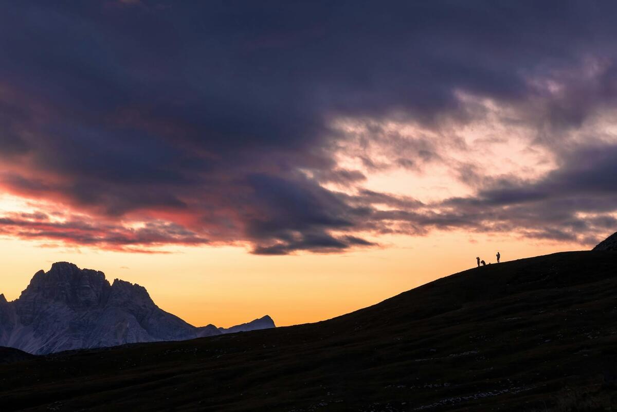 A picture of a sunset with silhouettes of 3 people in the distance on the hill.