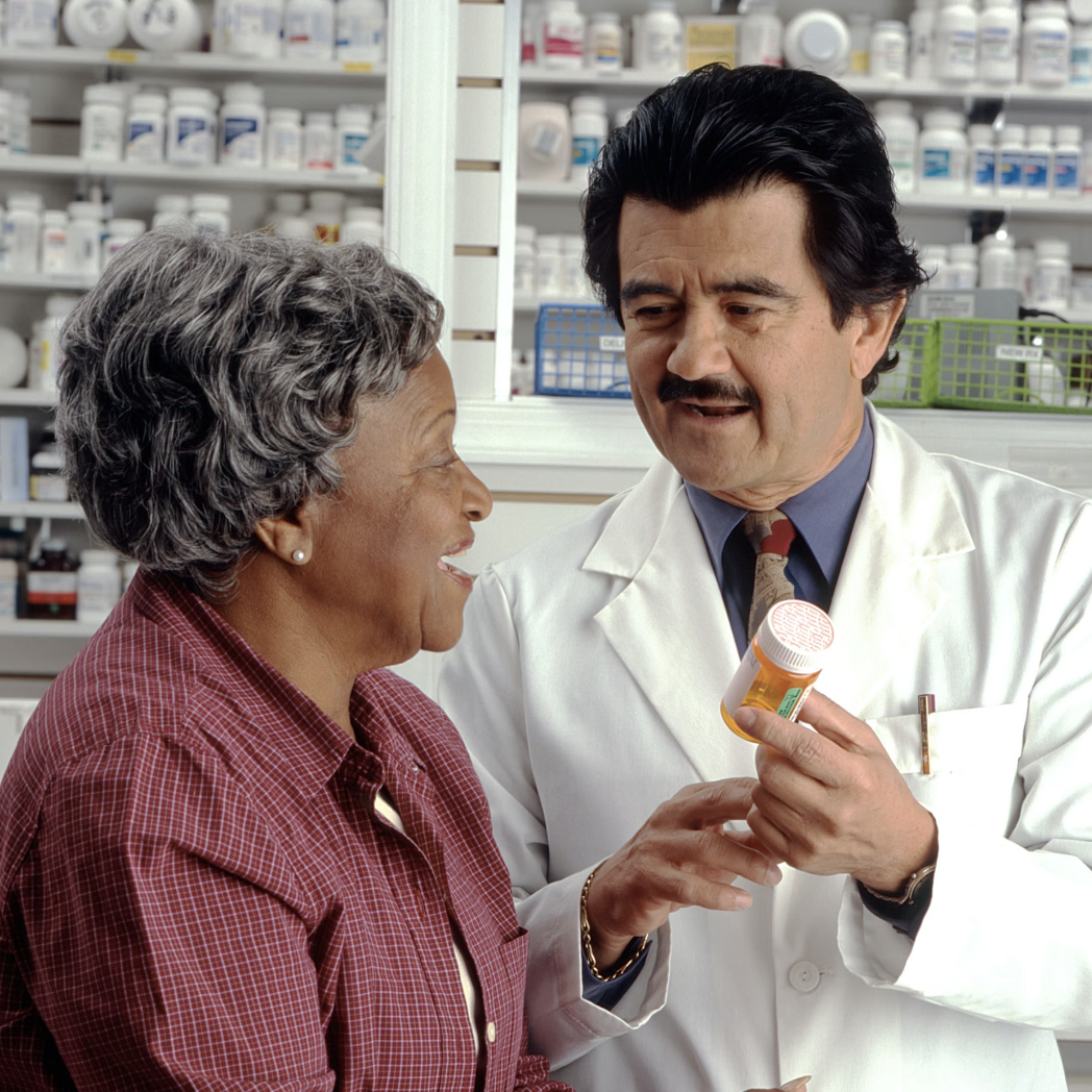 an older woman speaking to a pharmacist, who is holding an orange pill bottle