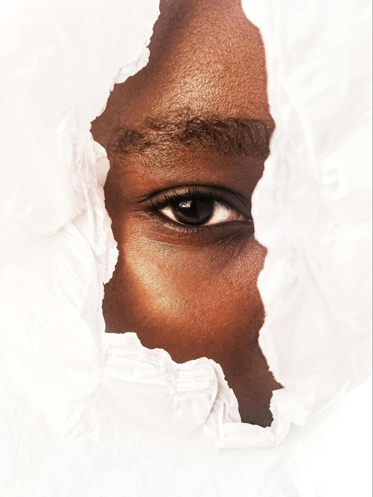 part of the face of a black person peeking through torn white paper
