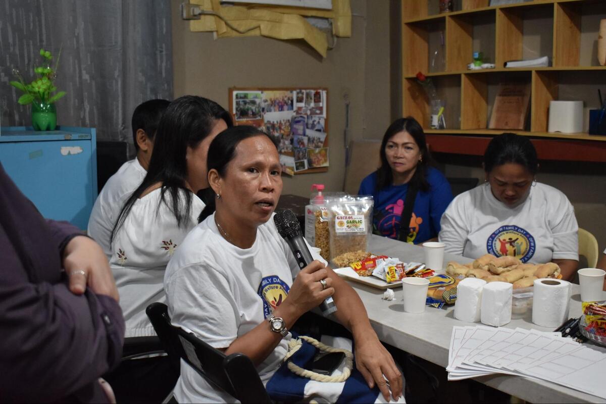 Group of Filipino women sitting at a table, centered on one who is turned from the table and holding a microphone