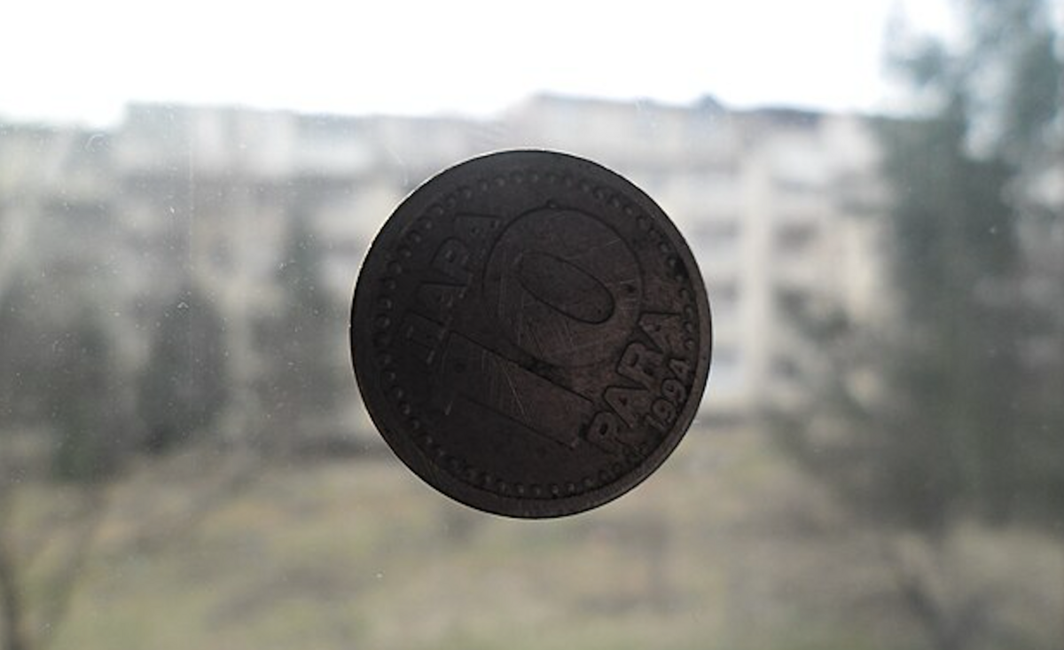 Image of a coin in the air, blurry background of trees and a building