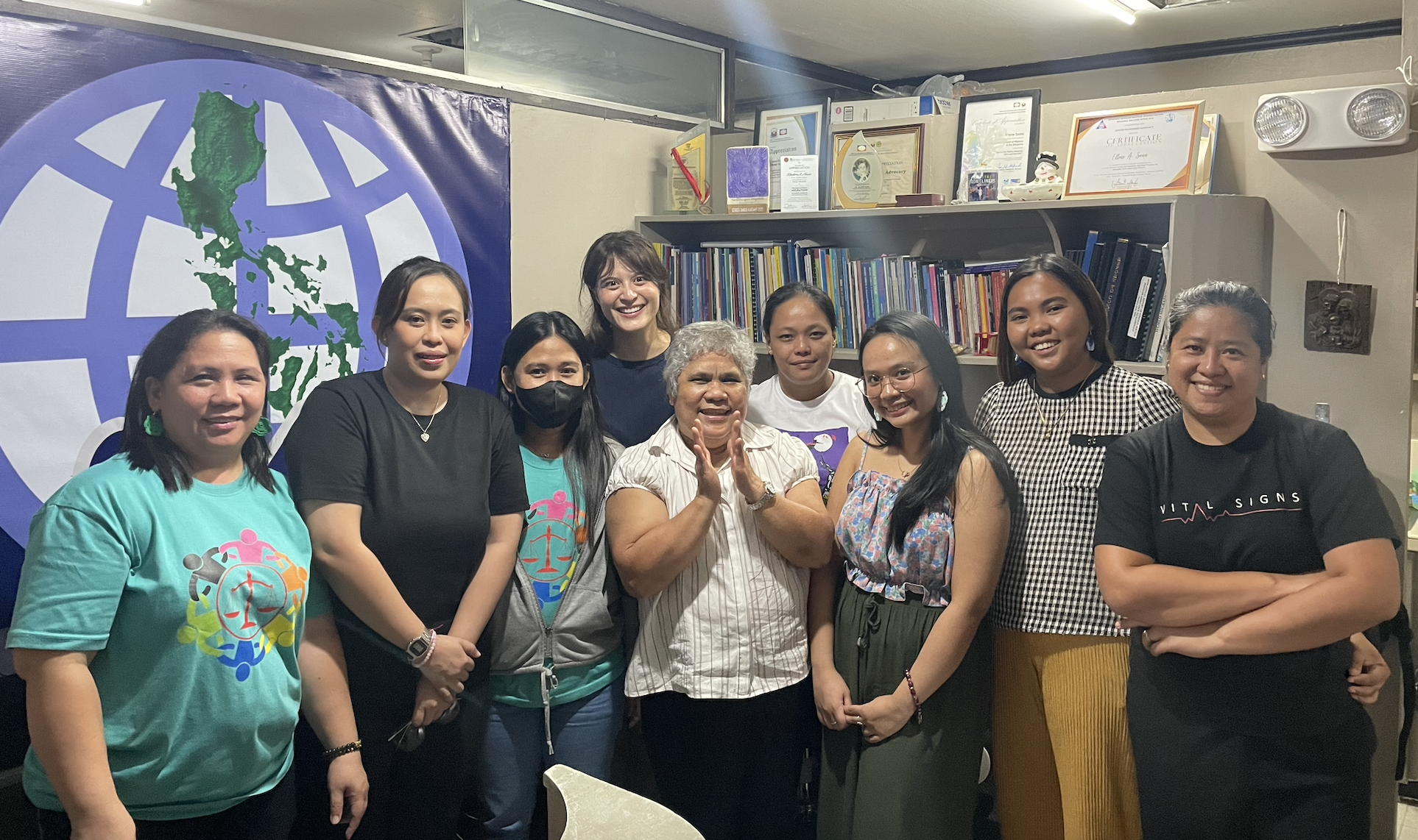 9 women stand together smiling at the camera. The Center for Migrant Advocacy staff and interns pose at the main office in Quezon City, Philippines.