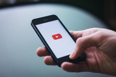 A picture of a hand holding a phone with the YouTube logo.